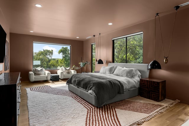Spacious primary bedroom with a sitting area and treeline windows.